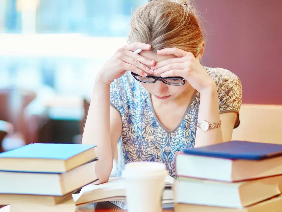 A stressed student studying, surrounded by books