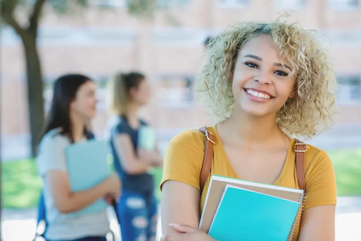 A smiling student on campus holding her books